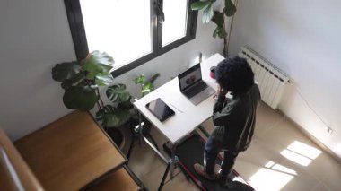 Bilgisayarlı, telefonlu, kulaklıklı, küçük bir koşu bandının üzerinde telefonda konuşan Afro-Amerikalı genç bir adam.