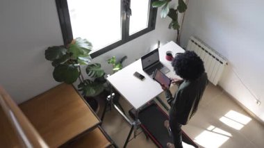 Bilgisayarlı, telefonlu, kulaklıklı genç Afro-Amerikalı adam küçük bir koşu bandının üzerinde masanın üzerinde tabletle birlikte.