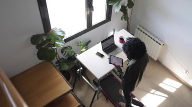 Bilgisayarlı, telefonlu, kulaklıklı genç Afro-Amerikalı adam küçük bir koşu bandının üzerinde masanın üzerinde tabletle birlikte.