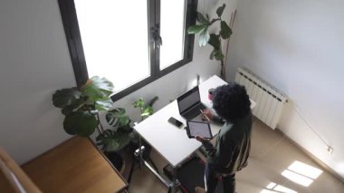 Bilgisayarlı, telefonlu, kulaklıklı genç Afro-Amerikalı adam küçük bir koşu bandının üzerinde masanın üzerinde tabletle birlikte.