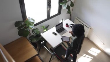 Bilgisayarlı, telefonlu, kulaklıklı genç Afro-Amerikalı adam küçük bir koşu bandının üzerinde masanın üzerinde tabletle birlikte.