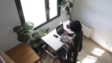Bilgisayarlı, telefonlu, kulaklıklı genç Afro-Amerikalı adam küçük bir koşu bandının üzerinde masanın üzerinde tabletle birlikte.