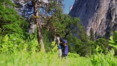 Anne ve iki küçük oğlu, güneşli ve sık ağaçlı bir ormanın içinden geçen dolambaçlı bir yolda yürürken görüldü. Sahne, Birleşik Devletler Ulusal Parkı 'nın nefes kesici doğal güzelliği içinde gözler önüne seriliyor.