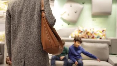 Çanta taşıyan bir kadın ve çocuklar modern bir mobilya galerisinde ev dekorasyonu seçeneklerini araştırıyorlar.