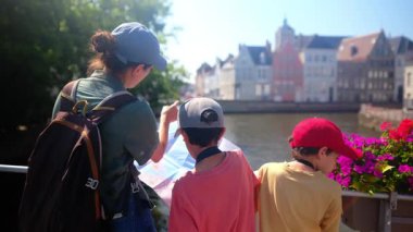 Su kenarında haritaya bakan bir kadın ve sevimli çocuklar..