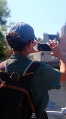 Şehirdeki deniz kenarındaki binaların yakınında fotoğraf çeken bir kadın.