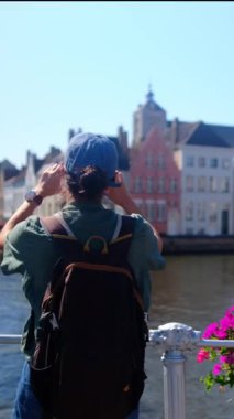 Şehirdeki deniz kenarındaki binaların yakınında fotoğraf çeken bir kadın.