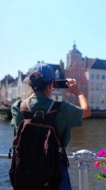 Şehirdeki deniz kenarındaki binaların yakınında fotoğraf çeken bir kadın.