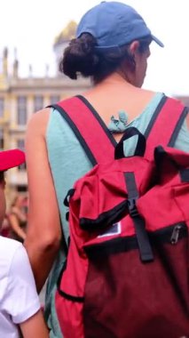 Kırmızı sırt çantalı bir kadın oğluyla şehirde yürüyor..