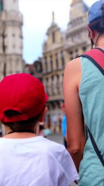 Kırmızı sırt çantalı bir kadın oğluyla şehirde yürüyor..