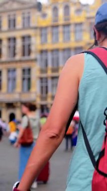 Kırmızı sırt çantalı bir kadın oğluyla şehirde yürüyor..