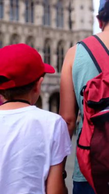 Kırmızı sırt çantalı bir kadın oğluyla şehirde yürüyor..