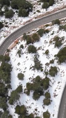 Karlı ve yemyeşil bir ormandan geçen sarmal dağ yolu.