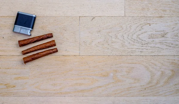 Three Tuscan cigars and a lighter on a wooden floor — Stock Photo, Image