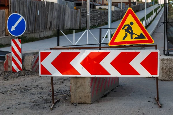 Work continues. Road works, road signs. Men at work. Some signage signs for work in progress on a city street. Barriers and road signs. Silhouette of a worker at work.