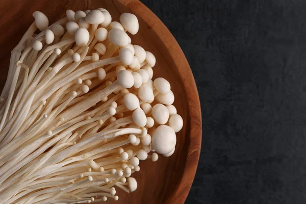 Enoki mushrooms over black background .Enokitake or enoki (Flammulina velutipes) white mushroom used i food and salads, also known by the name golden needle mushroom or lily mushroom.