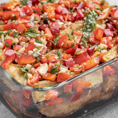 Akdeniz usulü kavrulmuş sebzeler, beyaz rustik bir masada, malzemelerle birlikte salata kasesinde. Beyaz arka planda kapari ve zeytinlerle kızartılmış sarı ve kırmızı biber salatası. Izgara sebze..