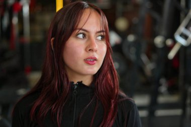 Kahverengi gözlü, spor salonuna odaklanmış ve kararlı bir şekilde bakan genç kızıl saçlı bir kadın, yakın çekim vesikalık taşınma ve sağlıklı bir yaşam tarzı.