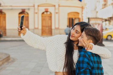Genç kadın ve küçük kardeşi gülümseyip barış işaretleri gösterirken akıllı telefonla güneşli bir sokak selfie 'si çekiyorlar ve birlikte kaygısız bir şehir anının tadını çıkarıyorlar.