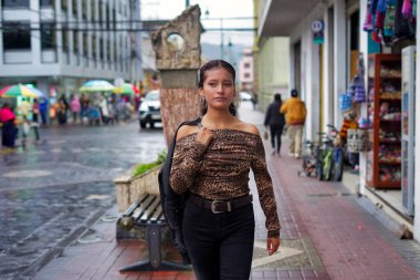 Yağmurlu bir günde, yağmurlu bir günde ceketi omzuna sarılı, leopar desenli bir bluz ve siyah bir pantolon giyerek güvenli bir şekilde şehir caddesinde yürüyen genç bir kadın.