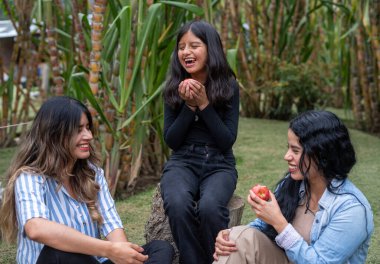 Parktaki güneşli bir piknik sırasında gülen ve elma paylaşan üç nesil kadın sağlıklı atıştırmalıkların, kaynaşmanın ve kaygısızlığın keyfini çıkarıyorlar.