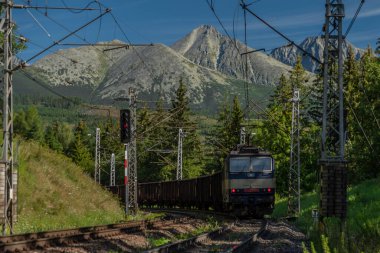 Yazın güneşli sabahlarda Vysoke Tatry dağlarının altında mavi elektrikli kargo treni