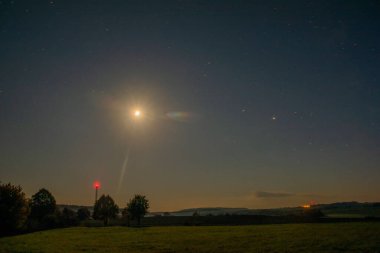 Çek Cumhuriyeti 'nin Utery kasabası yakınlarındaki çayır arazi ve tarlada yıldızlı koyu mavi gökyüzü ve ay ışığı