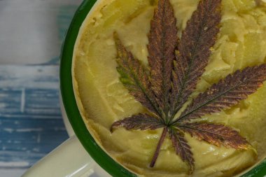 Ahşap masada yeşil ve menekşe marihuana yapraklarıyla marihuana yağlı metal renkli sürahi.