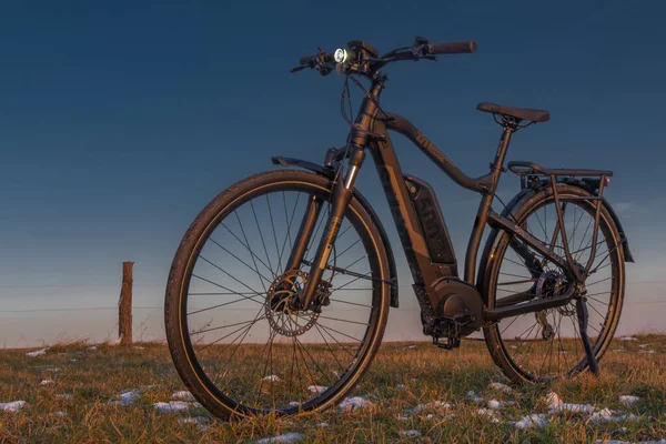 Güneş doğarken siyah ve gri elektrikli bisiklet. Buz gibi arazide sabah vakti. Sarı güneşli.