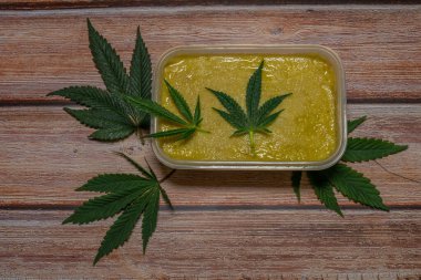 Ahşap masada marihuana yağı ve koyu yeşil yapraklar.