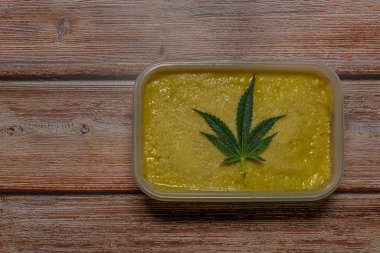 Ahşap masada marihuana yağı ve koyu yeşil yapraklar.