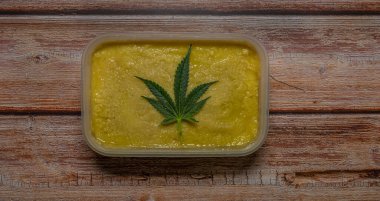 Ahşap masada marihuana yağı ve koyu yeşil yapraklar.