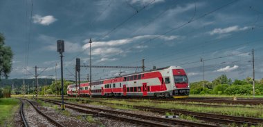 Kırmızı elektrikli lokomotifli yolcu treni ve yaz akşamları kırmızı yolcu vagonları.