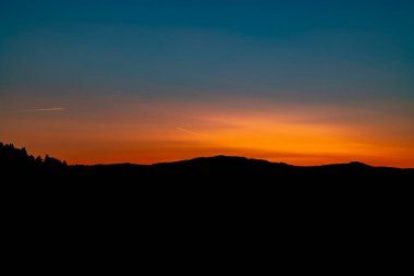 Soğuk kış sabahında gün doğumunun renkleriyle dağların ve ormanların silueti.