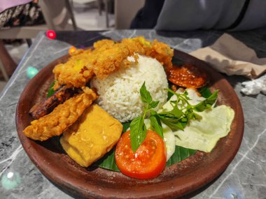 Delicious Indonesian smoked fish, rice, tempeh, tofu, and fresh vegetables on a traditional plate.