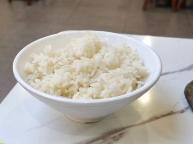 White rice in a bowl on a marble table at a food court with a blurred background.