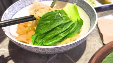 a person mixing and eating Mie Ayam, a popular Indonesian chicken noodle dish, in a patterned bowl.