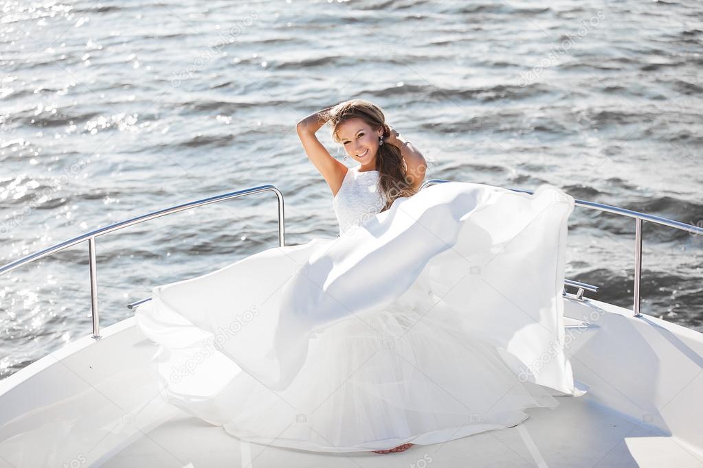 happy bride in a white wedding dress on a yacht sailing wind evolve her hair and dress