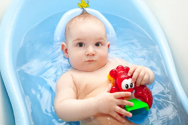 A small child is bathed in a blue bath toys . — Stock Photo, Image