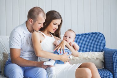 a young family with a nice and sweet little baby sitting on the sofa in a bright interior