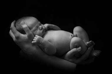 mutlu aile , genç anne kollarında yeni doğmuş bir bebek tutan ve yavaşça ona sarıldı, siyah bir arka plan üzerinde siyah beyaz fotoğraf .