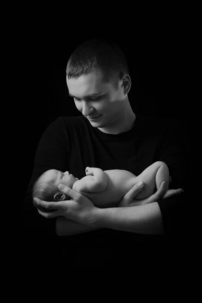 Familia feliz, padres jóvenes sosteniendo a un bebé recién nacido en sus brazos y suavemente lo abrazó, foto en blanco y negro sobre un fondo negro  . — Foto de Stock