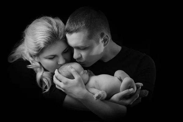 Famille heureuse, jeunes parents tenant un nouveau-né dans ses bras et le serrant doucement dans ses bras, photo en noir et blanc sur fond noir  . — Photo