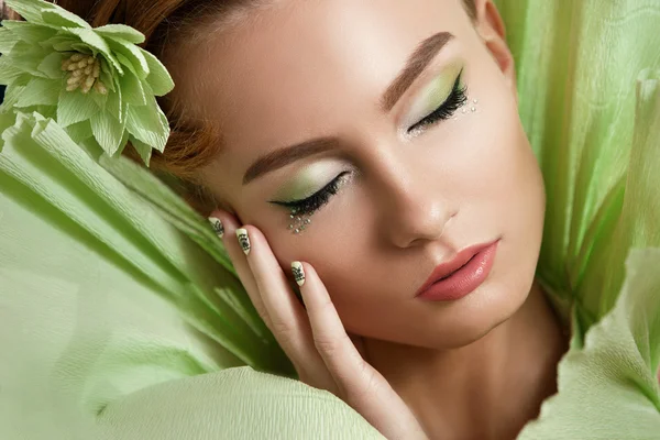 Belleza joven con maquillaje profesional y precheskoy, vestido verde, una flor en la mano, fotografiado en el estudio. Hermosa mujer  . — Foto de Stock