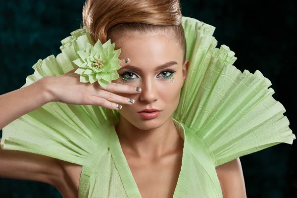 Belleza joven con maquillaje profesional y precheskoy, vestido verde, una flor en la mano, fotografiado en el estudio. Hermosa mujer  . — Foto de Stock