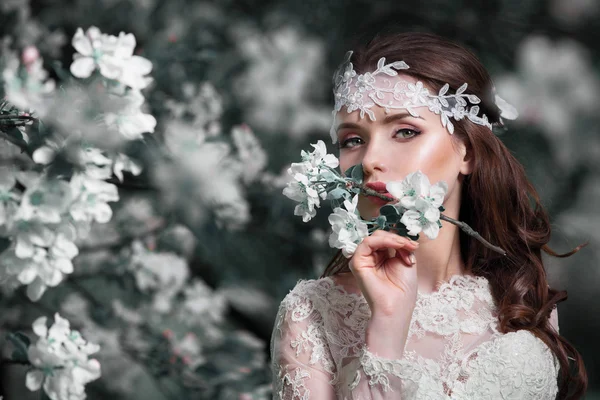 Schoonheid vrouw bruid in haar trouwjurk en decoratie in haar haar in een weelderige tuin van appels . — Stockfoto