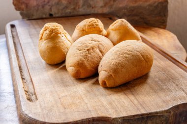 Taş duvara karşı ahşap yüzeyde altın hamurlu beş parça rustik ekmek sergileniyor. Konforlu mutfak ortamında geleneksel ev yapımı pişirme sergileniyor..