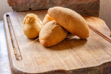 Ahşap kesim tahtasının üzerinde altın kabuklu dört parça rustik ekmek, konforlu ev yapımı pişirme sahnesinde yuvarlak ve oval şekiller.