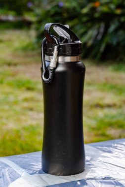 Açık havada plastik kaplı yüzeyde duran karabinalı siyah su şişesi..