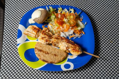 Izgara tavuk şişi, salata, ekmek ve patates rengarenk tabakta.